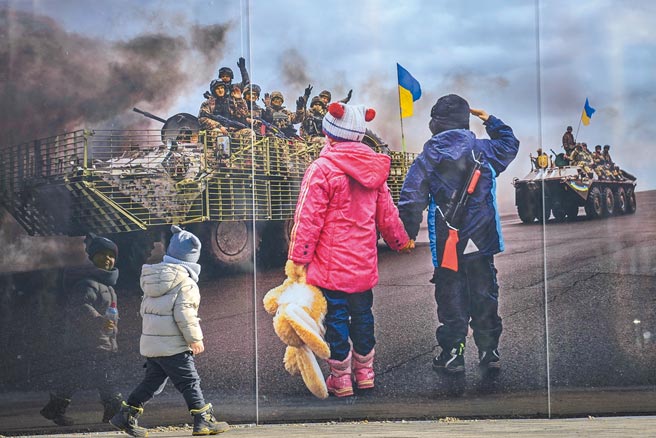 俄罗斯极可能入侵基辅，乌克兰已决议全国进入紧急状态。图为乌东地区一名儿童，经过战火受难者摄影纪念馆前，影像中的孩子向坦克车上的士兵敬礼致意。（美联社）