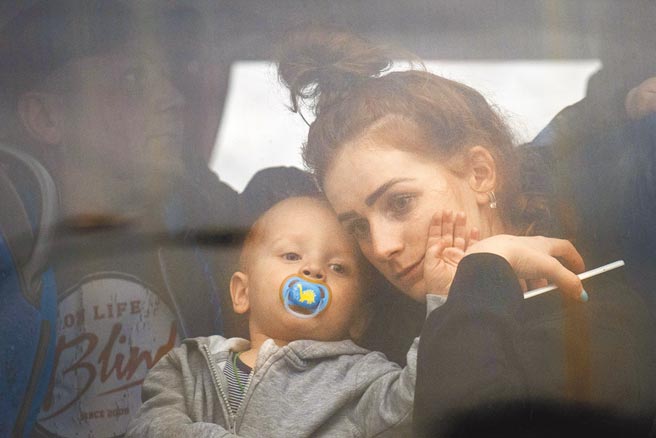 圖為烏克蘭婦女帶著小孩搭公車離開基輔時，無助看著窗外。（美聯社）