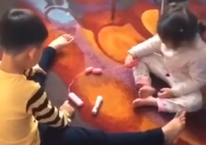 男女幼童在地上把玩1款「有線」玩具，該玩具一頭是圓形震動物體，一頭是遙控器，疑似就是「情趣用品」，孩子們將各自的震動球靠向對方，玩得不亦樂乎。（翻攝自臉書「爆廢公社公開版」）