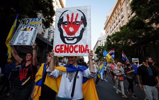 阿根廷一名抗议俄罗斯入侵乌克兰的民眾高举谴责普丁的画报，指责普丁像纳粹一样犯下种族屠杀罪行。（图／路透）