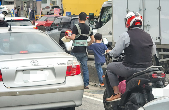網友在新北市五股見到一名父親「胸前背一個、手上牽一個」，帶著2個孩子穿梭車陣賣玉蘭花。（翻攝臉書《●【爆廢公社二館】●》）