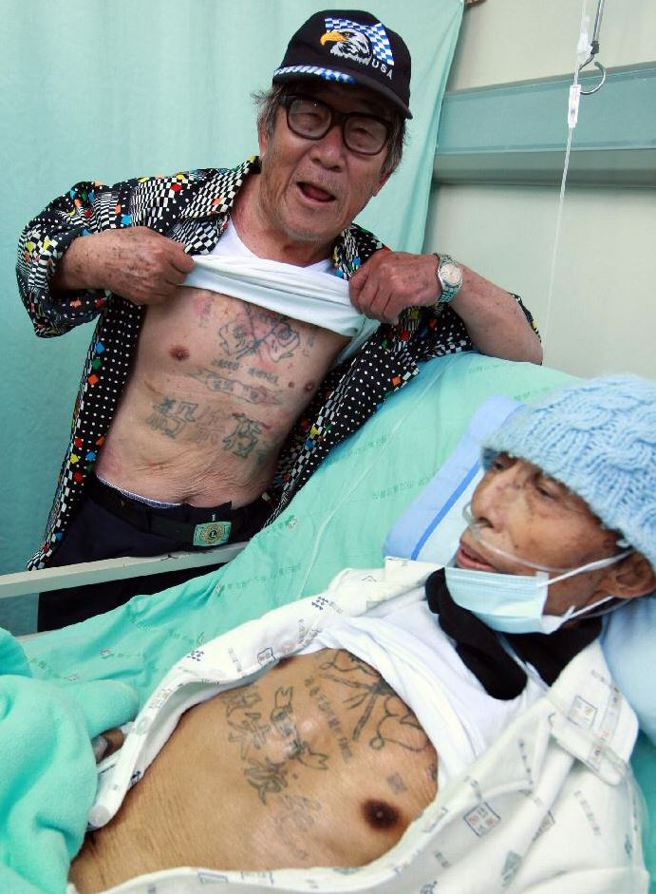 17岁被国民党抓兵离开河南老家，国共内战后被抓又成了「八路军（解放军）」，韩战爆发时志愿军过鸭绿江「抗美援朝」，弹尽援绝成了俘虏，在济州岛美军克难战俘营待了三年，后选择来台，成了「反共义士」。度过荒谬及悲伤的时代，老兵未凋零的也都已80多岁，岳振班长（万芳医院病床）、徐公亲（立者）拉开衣服露出「杀朱拔毛」及党国旗的刺青，述说当年的亲身经歷，感受在心比刺青还深刻。（郑履中摄）