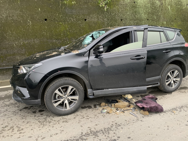 休旅車被落石砸破擋風玻璃，駕駛當場開放性骨折；事故照中，休旅車玻璃破出驚悚大洞，一旁的車身零件還有血跡。（翻攝照片）