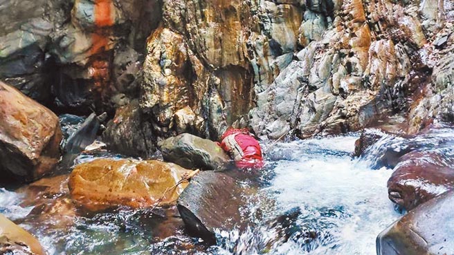 林女獨攀南投縣信義鄉玉山北北峰和對關山失聯，23日在1處溪谷上方約30公尺平台尋獲，不幸已成冰冷大體。搜救人員將遺體移至溪床，再以接力方式搬運至停車場。(消防局提供/吳建輝南投傳真)