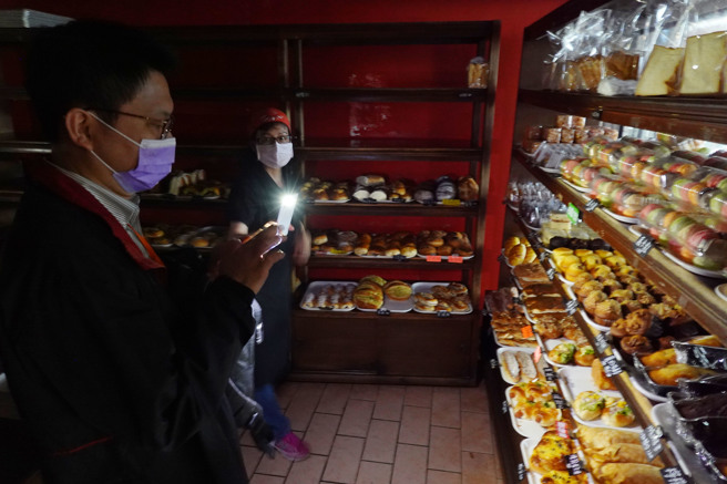 台北市士林捷运站附近商圈30日晚间发生停电状况，麵包店内的顾客靠着手机灯光选购麵包。（姚志平摄）