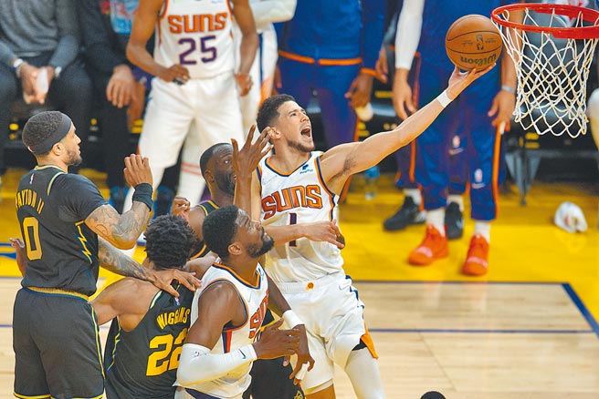 太阳戴文布克（右）在勇士防守下飞身左手上篮，布克此役手感不佳，但凭藉着犯规获得多次罚球机会取分。（美联社）