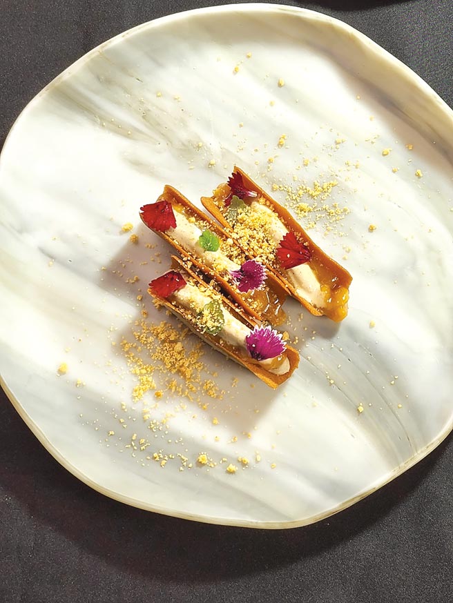 〈焦糖香蕉慕斯〉是将脆饼制作成船身造型，脆饼里面放入香蕉慕斯、焦糖香蕉加上泰式茶叶制作的泰奶冰淇淋，再以山萝卜叶、小菊花、石竹增添甜美香气。图／姚舜