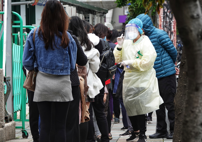 连续4天本土病例破百，台北医院的社区筛检站外有不少民眾排队等候，工作人员身穿全套防护装备协助民眾报到採检。(黄世麒摄)