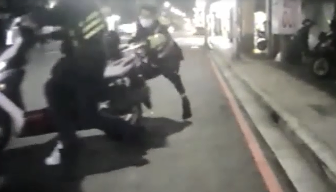 邱姓员警骑着摩托车接受盘查，过程中竟准备驶离，随即遭2名「自己人」制止，其中1人试图抓龙头，反被拖着走，另1名员警则在后方拉住车尾，同样遭拖行。（翻摄画面）