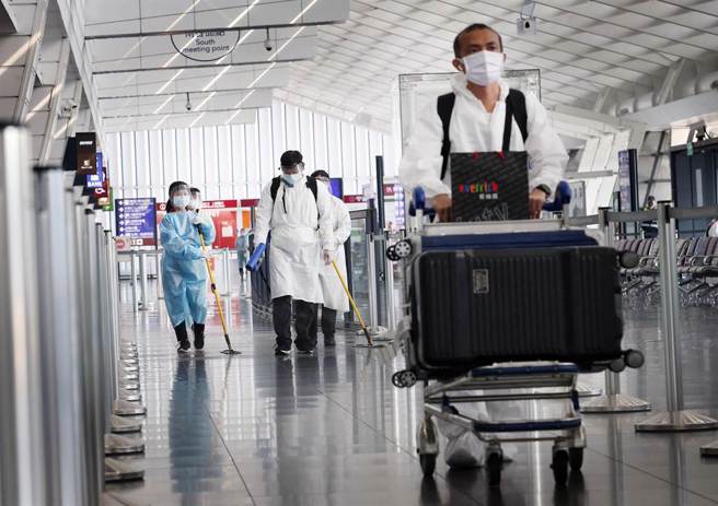 在桃園機場第一航廈入境大廳內，身穿防護衣的旅客準備搭車離開，清潔人員在後方消毒環境。（范揚光攝）
