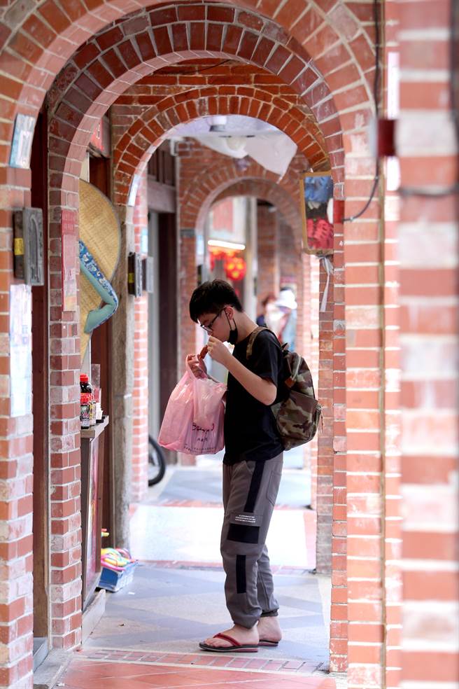 民眾在新北市的深坑老街买了小吃，特地远离人群才脱下口罩品尝美食。（黄世麒摄）