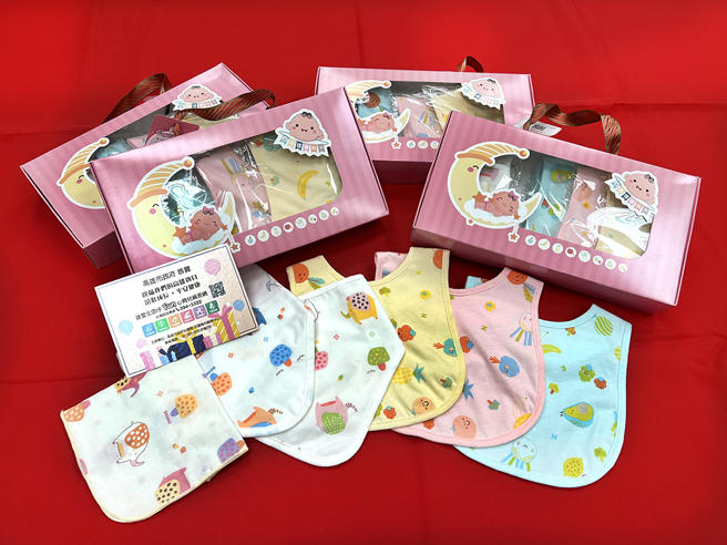 新生兒禮包內有育兒資訊、三角口水巾、圍兜、手帕等小物。設計有可愛動物及高雄特有蔬果物產，香蕉、鳳梨、番茄等圖案。(圖片提供/高雄市政府社會局)
