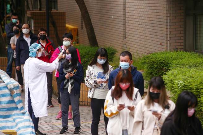 国内疫情持续升温，有民眾一早就到关渡医院筛检站进行採检，採检前医护人员穿梭队伍中帮忙量额温。（邓博仁摄）