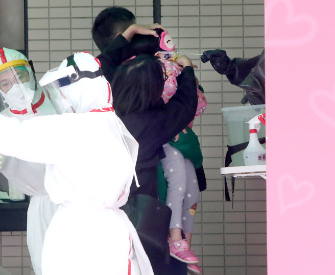 国内疫情严峻，儿童染疫后可能出现的症状也受家长关注。图为家长带孩子至快筛站筛检。（图／郑任南摄）