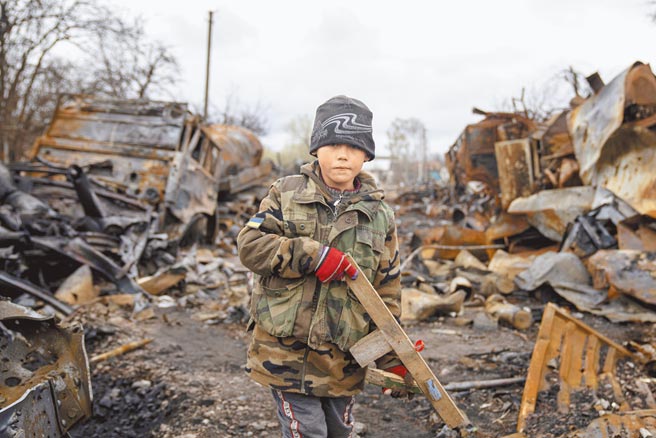 俄乌战争仍在持续，乌克兰的切尔尼戈夫（Chernihiv）多处成为焦土，一名7岁的乌克兰男孩手持一把木制玩具步枪，身旁不远处是已损毁的俄国军车。（美联社）
