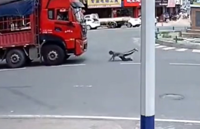 大陸江西省一名男子意圖假車禍碰瓷，慢動作衝向大貨車後倒在道路上。（翻攝自微博）