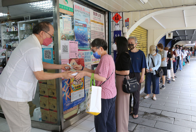 「快篩實名制」開賣第二天，每次可憑健保卡或居留證就能到藥局買一組5入500元的快篩試劑，29日民眾一早前往藥局排隊搶購，為保持社交安全距離，藥師在店門口直接讓民眾購買。（陳俊吉攝）
