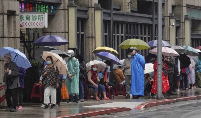 新冠肺炎疫情持續擴大，即便下雨，大家也撐傘在藥局門口排隊買快篩。（黃子明攝）
