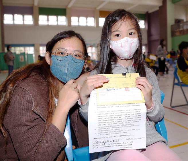 新冠肺炎疫苗日前開始為6-11歲學童接種，桃園市龜山區自強國小3日施打莫德納疫苗，一位中年級學童在休息區與陪伴的媽媽秀出小黃卡。(陳怡誠攝)