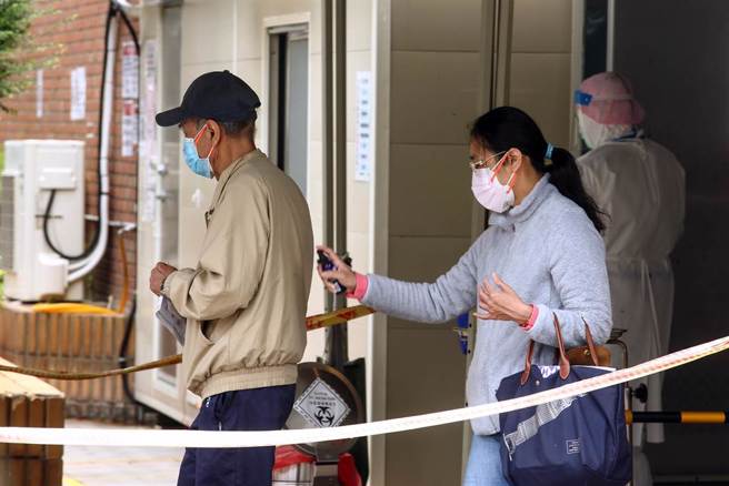 教育部日前宣布校園因應COVID-19防疫授課方式調整實施原則，並自8日起實施。8日母親節當天有民眾戴著雙層口罩前往關渡醫院採檢，採檢完身旁家人拿著酒精做清消。（鄧博仁攝）
