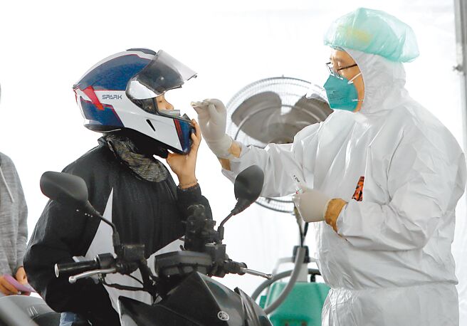 北士科快筛阳车来速筛检站，15日持续提供快筛阳性者PCR筛检与拿药服务，一位骑机车的民眾掀开安全帽接受採检。（郑任南摄）