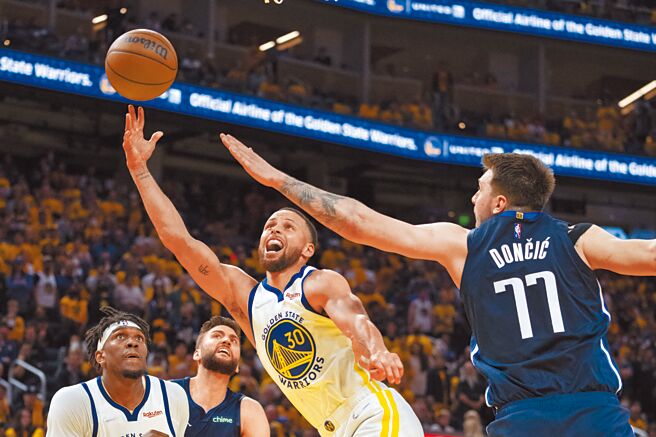 勇士射手柯瑞（中）閃過獨行俠前鋒東契奇（右）的左掌封阻以右手挑籃。（路透）