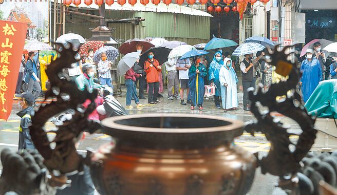 下周二滞留锋又接近，各地可能有大雨发生。图为台北市松山霞海城隍庙免费发放新冠肺炎快筛试剂，民眾冒雨排队等候领取。（资料照 郑任南摄）
