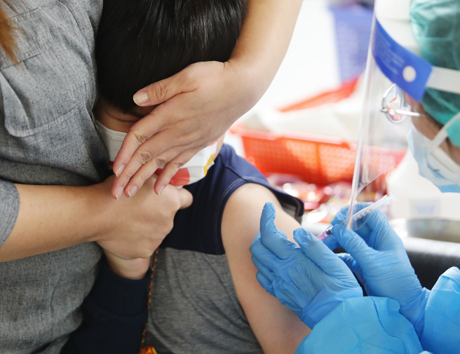 设在中正纪念堂设立的大型儿童疫苗接种站，4日家长带着小朋友前往施打疫苗，并用手帮小朋友遮脸完成注射。（季志翔摄）