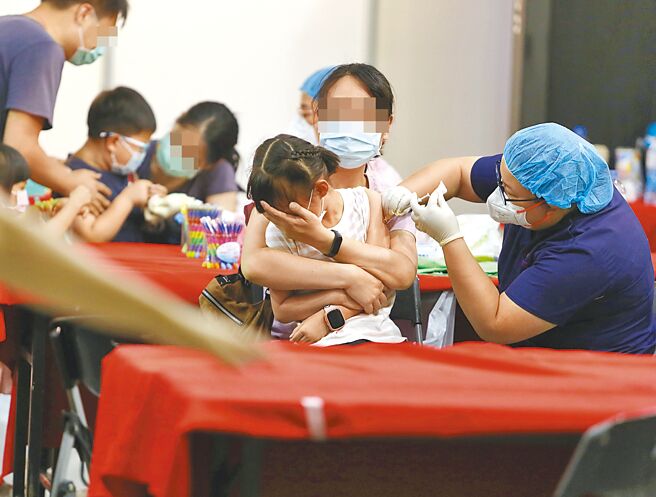 一位家长用手摀住小孩的脸，减轻小孩看到打针针头的恐惧感。（本报资料照片）
