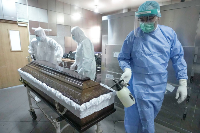 图为罗马尼亚殡葬人员消毒新冠死者的棺木。（图／美联社）