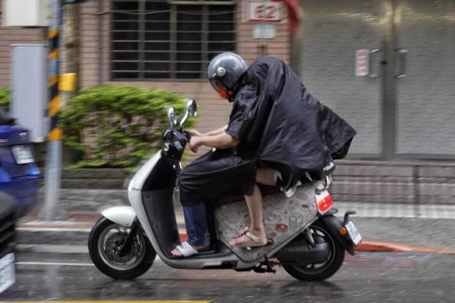 氣象專家賈新興表示，預估7月21日開始環境有利颱風生成，圖為突然下雨兩人共用一件雨衣。（報系資料照）