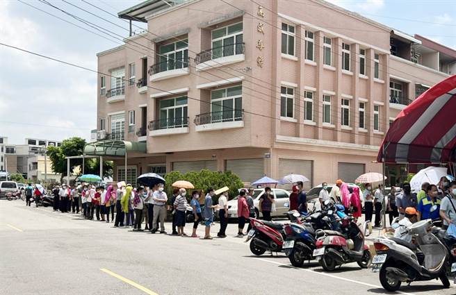 神冈区社口活动中心，今天上午民眾在艳阳烈日下撑伞大排长龙等候施打。（市议员周永鸿服务处提供）