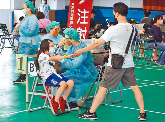 北市铭传国小23日进行第2剂儿童新冠肺炎疫苗施打作业，一位家长一手拿着手机拍摄留念，另一手牵着小朋友的手给予勇气与安慰。（姚志平摄）