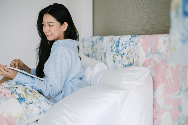 （诚品行旅的「羽后新生｜永续漫游」主题客房，以粉色、蓝色系的印花布料点缀，透过不对称的拼接手法，装饰于房内的床头板、灯罩、花器及抱枕。图／诚品行旅提供）