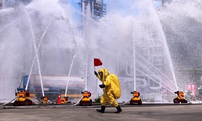 「全民防卫动员暨灾害防救（民安8号）演习」14日在新北市泰山塭仔圳重划区举行，实兵演练模拟共军导弹击中台北港，造成关键设施毁损，化学槽气体外泄，消防局出动灭火机器人等智能防灾科技投入抢救行列，救灾人员穿着全套化学毒灾防护衣，手举红旗警示。（黄世麒摄）