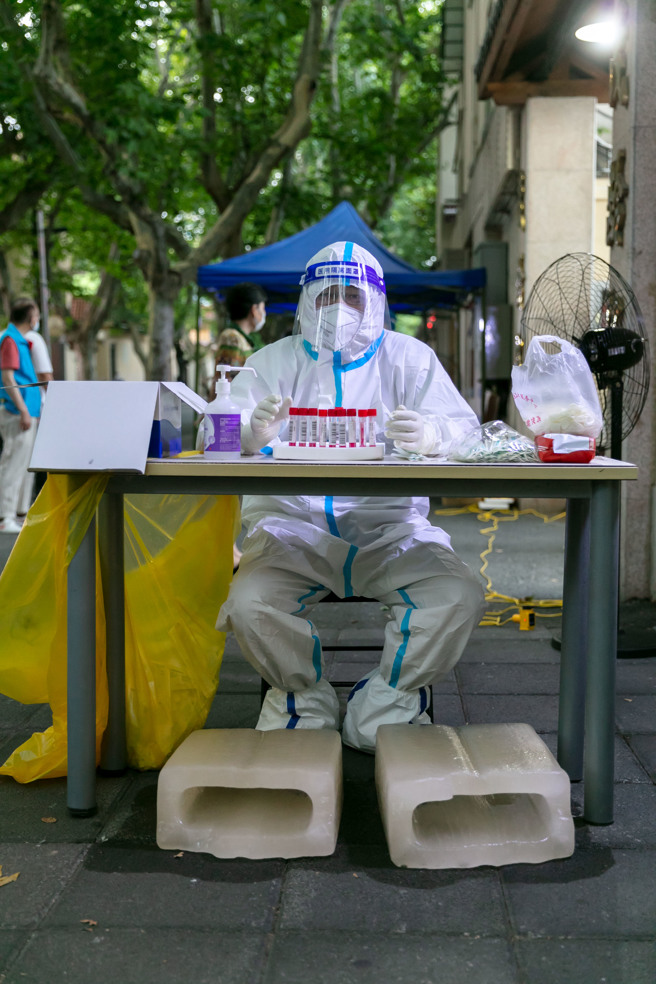 大陆数个城市气温飙高到40℃，防疫工作人员酷热下全身防护服难以忍受，有的还在桌底下垫着冰块，但中暑的风险仍极高。（图／新华社）