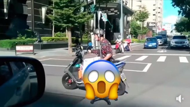网友在路上目击惊悚一目，居然有骑士单手骑车，另一手还紧握着点滴架。（图／撷取自爆废公社）