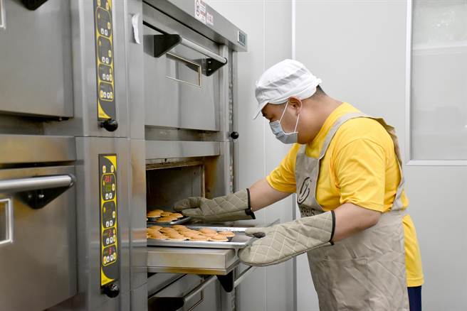 近日訂單陸續進來，憨兒們精神百倍，每個人聚精會神做好自己的工作，圖為憨兒將月餅送進烤箱。（林雅惠攝）