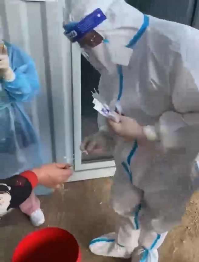 渔民拿着一只虾，核酸採样人员很费力地要从虾嘴上进行採样。网民问道：如果是贝类是否一颗颗撬开来採样？（图／微博）