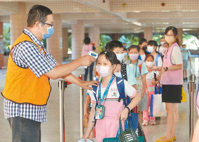 全国中小学30日开学，新北市光復国小工作人员帮戴口罩的小学生量测额温，落实校园防疫规定。（刘宗龙摄）