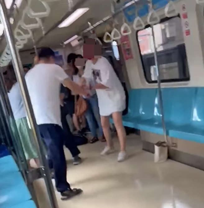 白色女子拿着红色长雨伞制止座位上男子往前攻击。(翻摄脸书爆料公社)