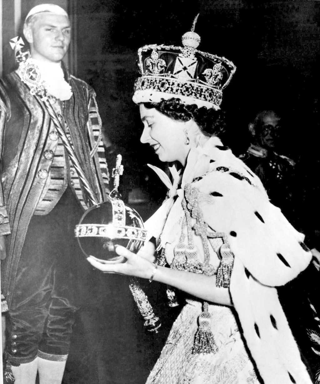 1953年6月2日的檔案照片中，英國女王伊麗莎白二世戴著鑲有寶石的皇冠，手持帶十字架的寶珠和權杖，在她的加冕儀式結束時離開倫敦威斯敏斯特教堂。（美聯社）