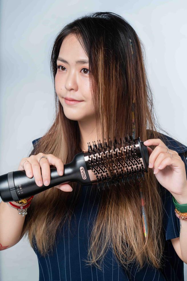 使用以TYMO VOLUMIZER负离子热风梳打造造型时，可一手扶着髮尾卷进造型器的齿梳中，最后稍微往前拉，打造滑顺又有弧度的直髮造型。（石智中摄）