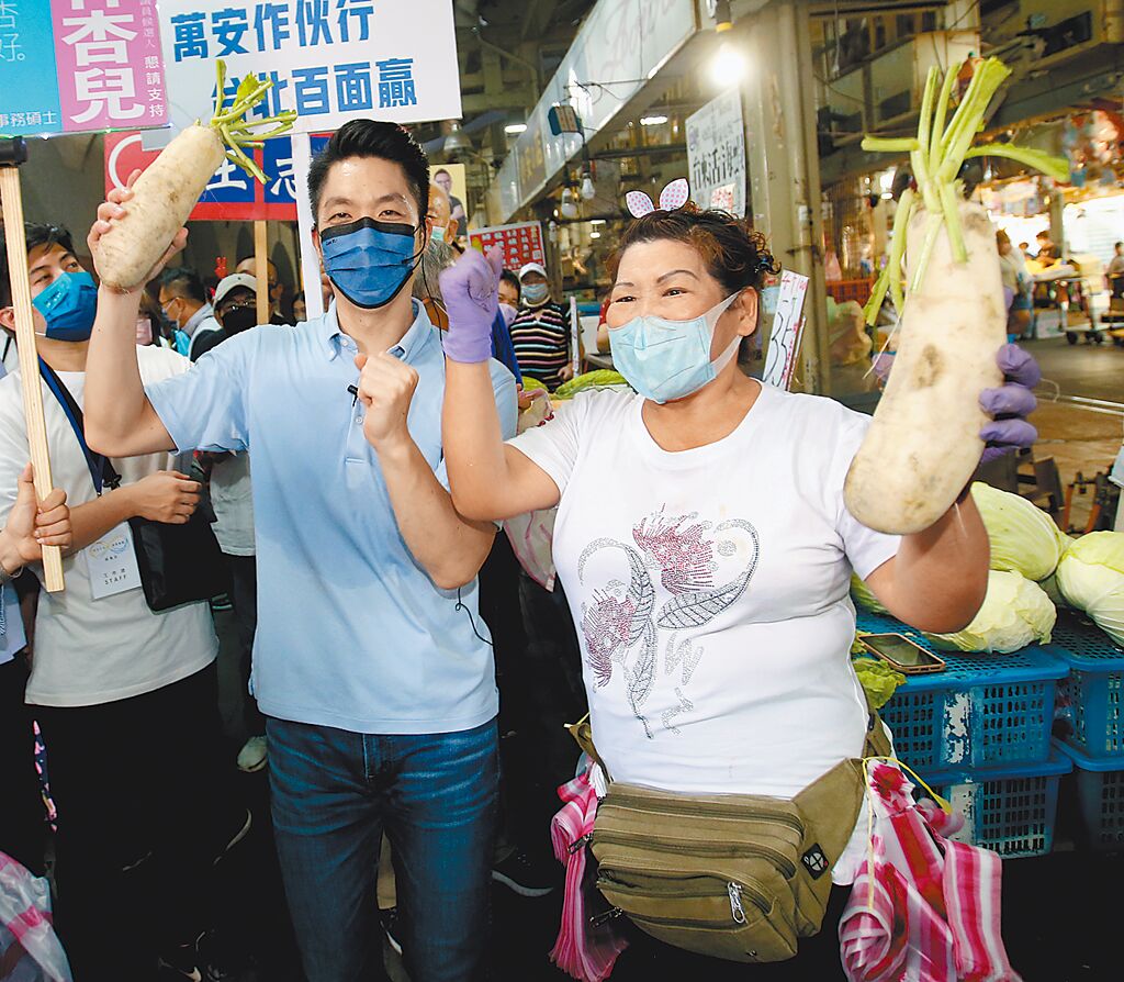 國民黨台北市長參選人蔣萬安（左）14日到綠營票倉士林市場掃街，和攤販拿著好彩頭的蘿蔔搏感情。（陳君瑋攝）