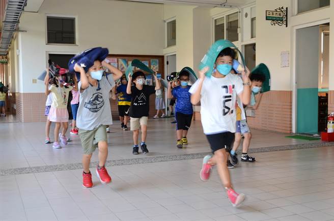 模拟芮氏规模4地震，高雄市冈山区寿天国小学童拿着书包与垫板当护具往操场移动，避免头部受伤。（林瑞益摄）
