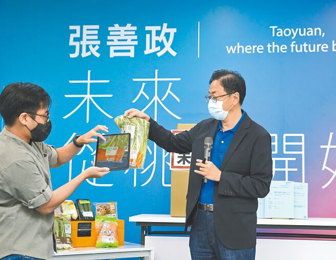 国民党桃园市长参选人张善政（右）21日拿着蔬菜包装外的QRcode，指这正是当年该研究案衍生作法，让消费者清楚掌控蔬果的生产履歷。（陈怡诚摄）