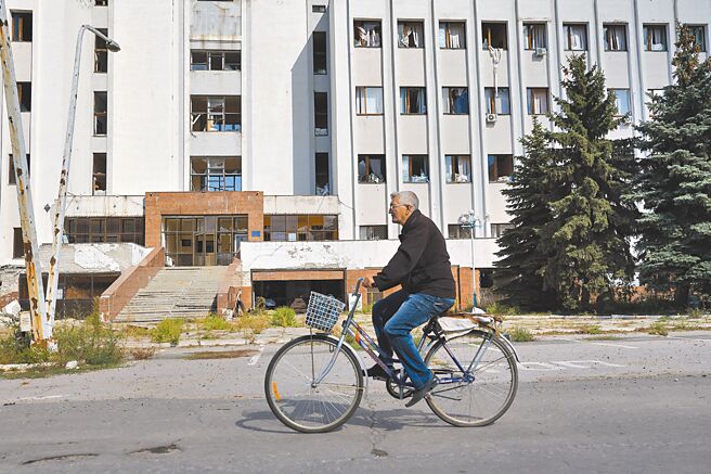 在盧甘斯克地區，一名男子騎車經過受損建築。（新華社）