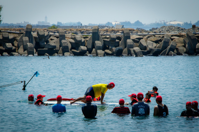 高科大师培中心教练群带领学员分组教学，说明遇到落水意外该如何自救。图为利用SUP板制造落水情境，实际演练自救方法。(照片/高科大提供)