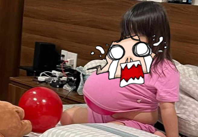 1名小女童被发现坐在床上，把气球塞进衣服内，形成「小小假孕妇」，但其实气球是「手机架」，小女童把手机放在气球上，忘神地盯着萤幕。（翻摄自脸书「爆废公社」）