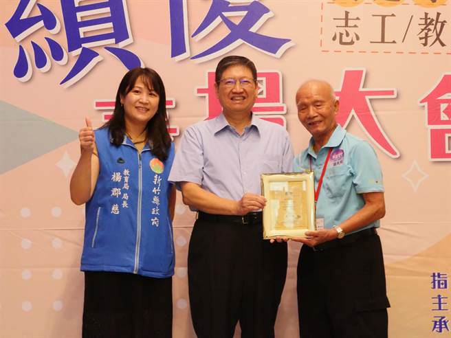 新竹县长杨文科（中）表扬最年长的导护志工罗美瑜（右），感谢他每天守护孩童。（新竹县府提供／邱立雅竹县传真）